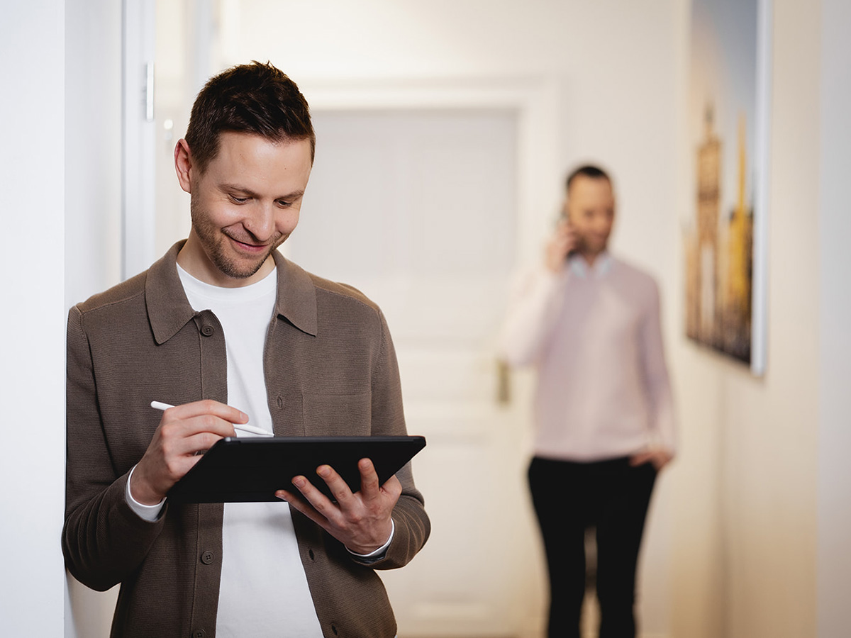Michael Fürgut arbeitet im Büro an einem Tablet, während Sebastian Fischer im Hintergrund telefoniert – digitale Steuerberatung im Arbeitsalltag
